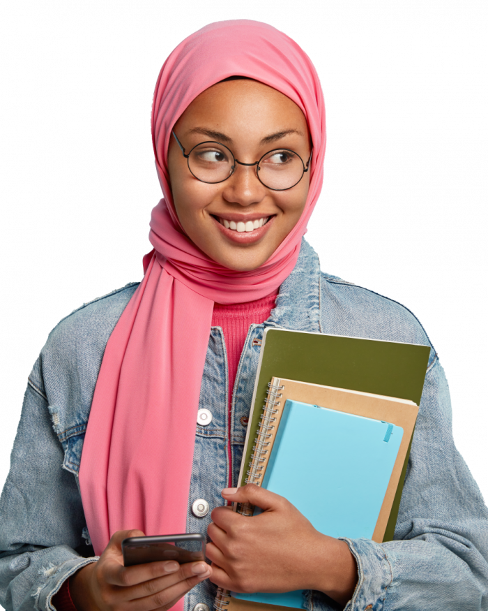 delighted-happy-muslim-student-types-messages-cell-phone-carries-notepad-focused-aside-with-joyful-expression-wears-jean-jacket-isolated-against-blue-wall-reads-interesting-article